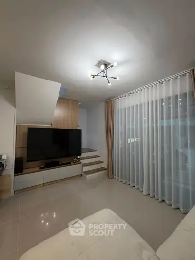 Modern living room with sleek design and large TV, featuring elegant curtains and stylish lighting.