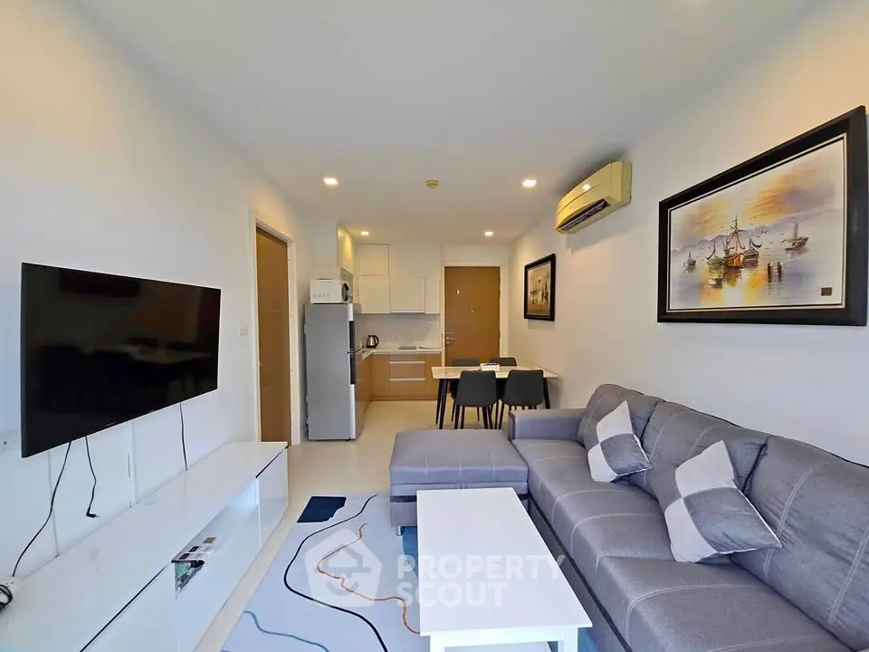 Modern living room with stylish decor, cozy gray sofa, wall-mounted TV, and open kitchen layout.