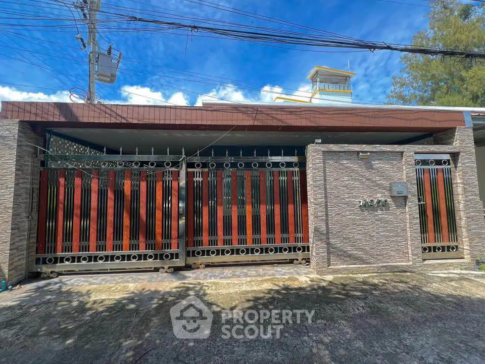 Modern gated entrance with stylish metalwork and stone facade under clear blue sky.