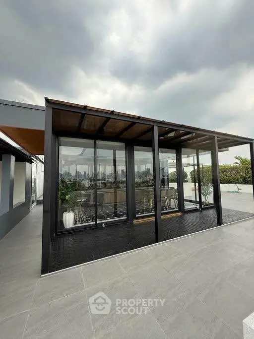 Modern rooftop terrace with glass enclosure and city skyline view, perfect for relaxation and gatherings.