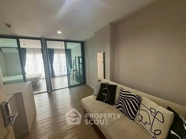 Modern living room with stylish decor and view into bedroom through glass doors.