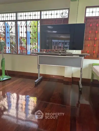 Spacious living room with polished wooden floors and large windows, featuring a modern TV stand.