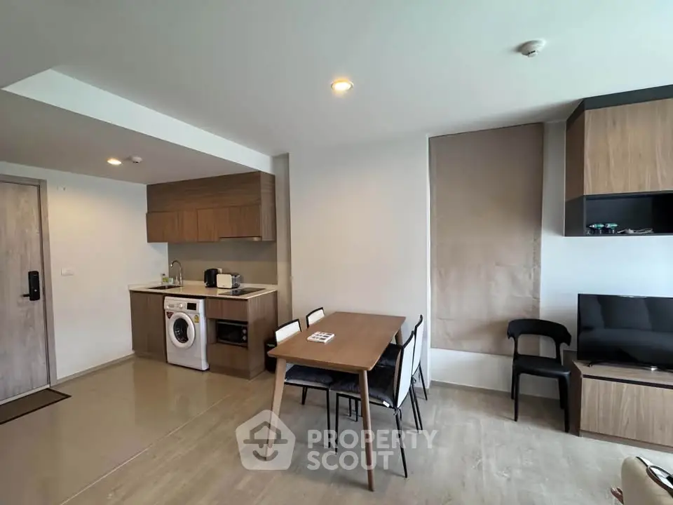 Modern open-plan living area with kitchen and dining space, featuring sleek wooden cabinetry and integrated appliances.