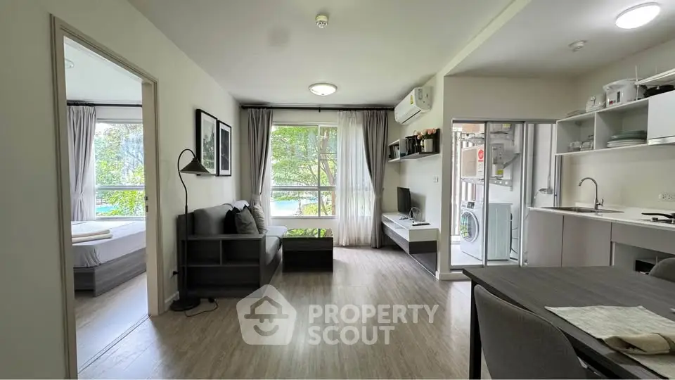 Modern open-plan living room with kitchen and bedroom view, featuring large windows and stylish decor.