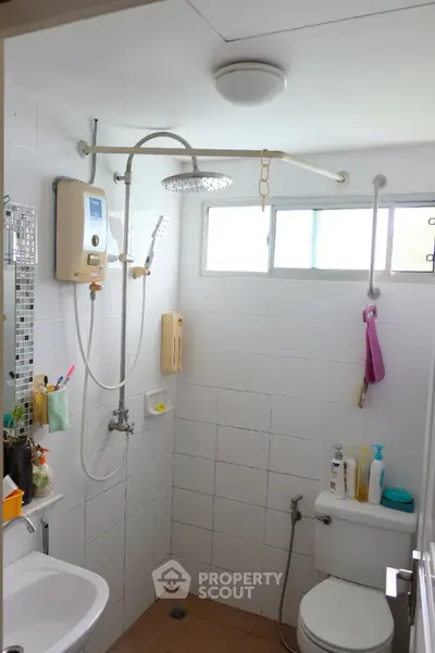 Compact bathroom with shower, toilet, and window for natural light, featuring modern fixtures and tiled walls.