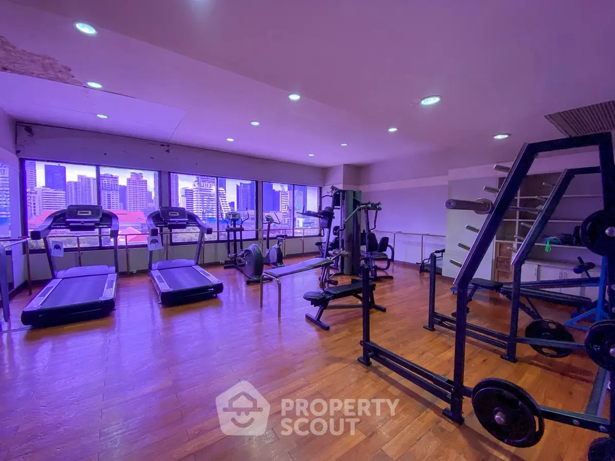 Spacious gym with modern equipment and city view, perfect for fitness enthusiasts.