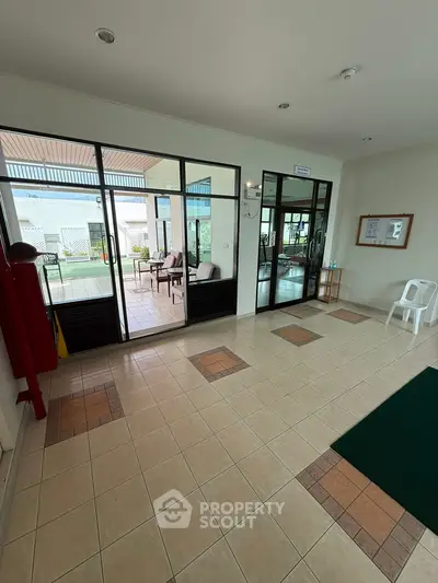 Spacious building entrance with tiled flooring and glass doors leading to a furnished patio area.