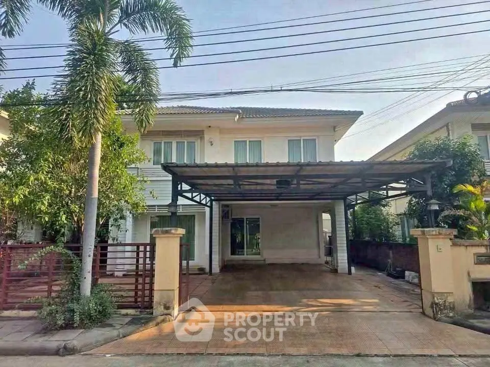 Charming two-story house with spacious carport and lush greenery in a serene neighborhood.