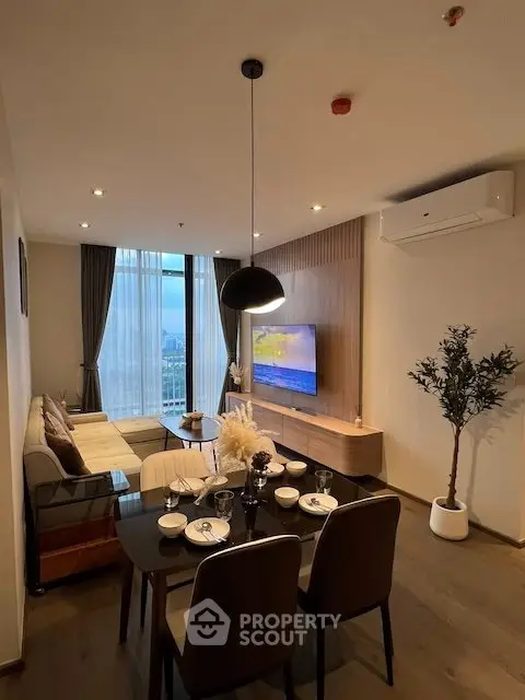 Modern living room with dining area, stylish decor, and large window offering city view.
