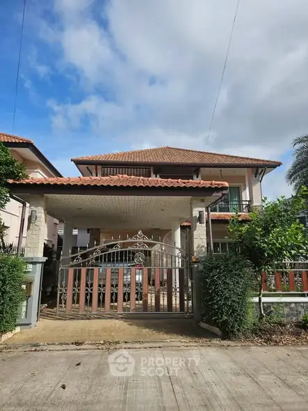 Charming two-story house with gated entrance and lush greenery under a clear blue sky.