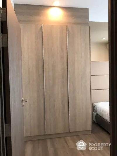 Modern bedroom featuring a large wooden wardrobe with ample storage, complemented by warm lighting and a cozy bed peeking from the side.