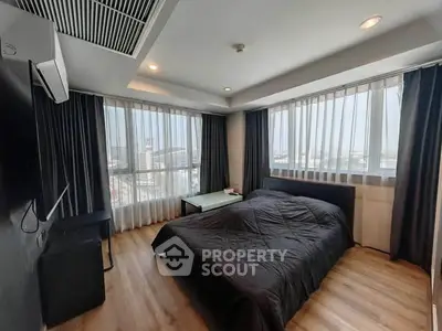 Modern bedroom with large windows and city view, featuring sleek black furnishings and wooden flooring.