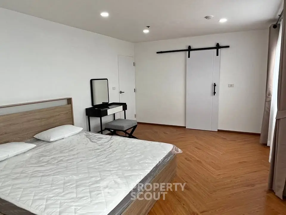 Spacious bedroom with modern design and sliding barn door, featuring a cozy bed and stylish vanity.