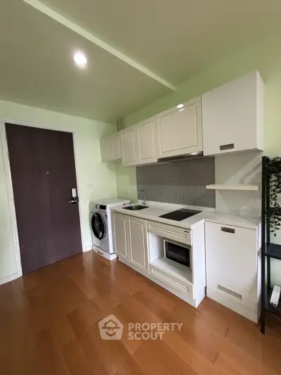 Compact kitchen with modern appliances and wooden flooring in cozy apartment