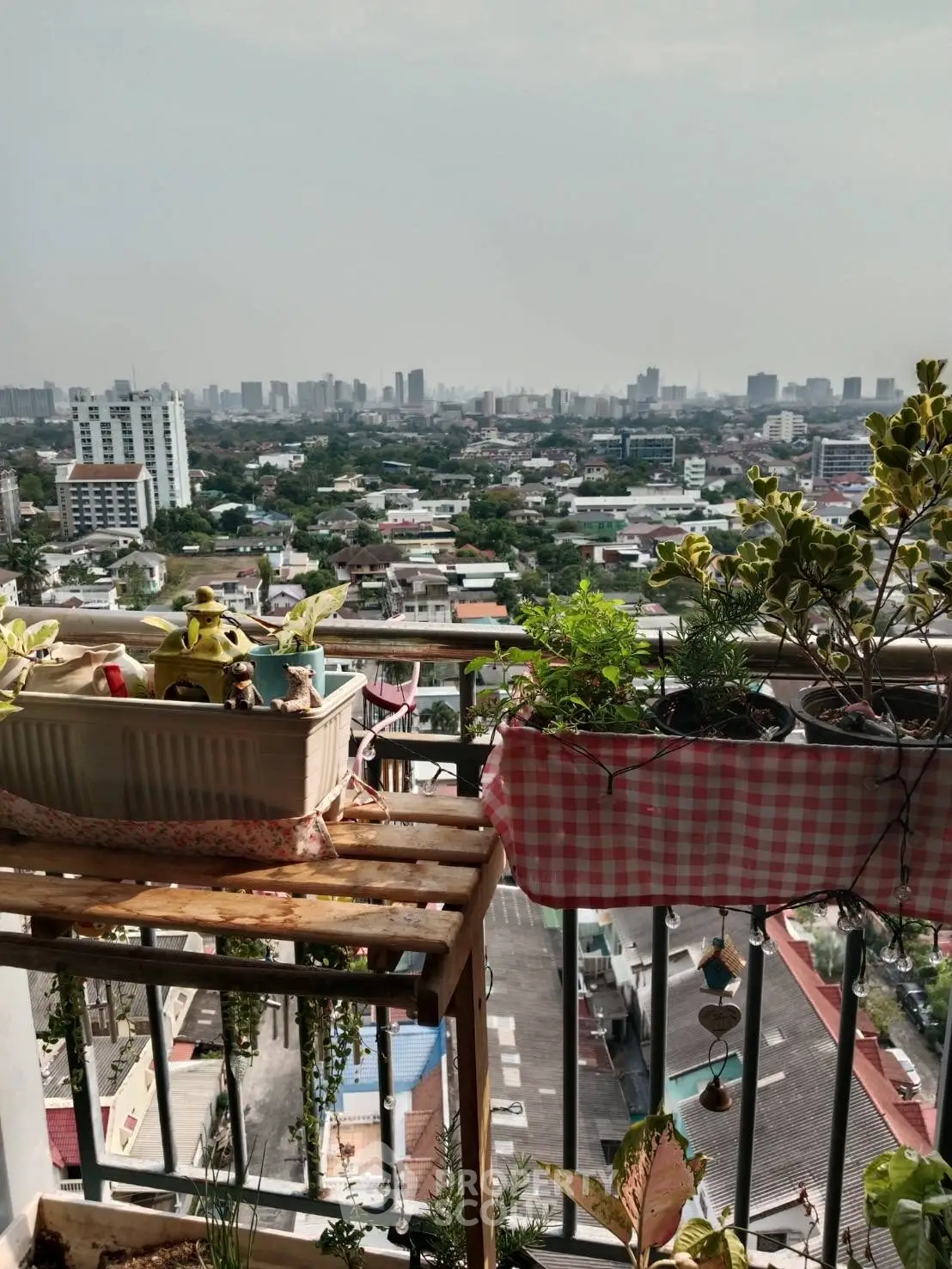 Stunning cityscape view from a high-rise balcony with lush plants and urban skyline.