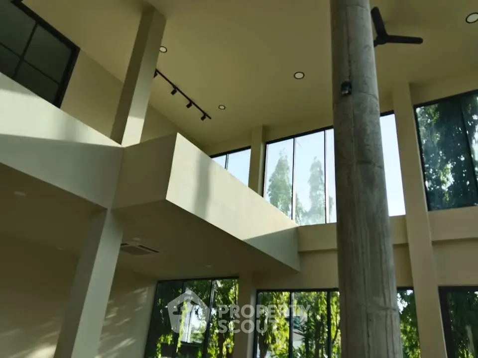 Spacious modern interior with high ceilings and large windows offering lush green views.