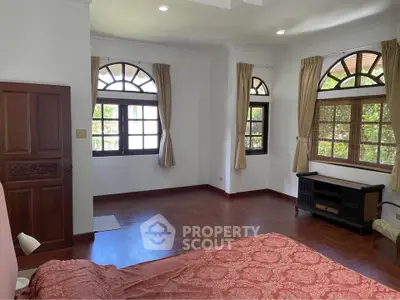 Spacious bedroom with elegant wooden flooring and large windows offering natural light.