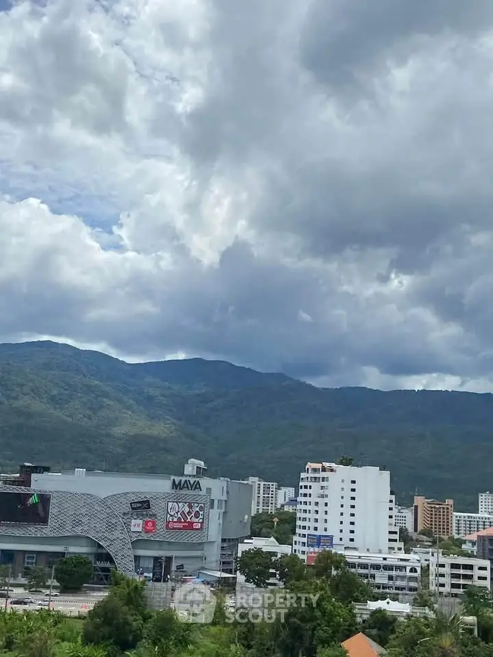 Scenic view of cityscape with mountains and modern buildings under cloudy sky.