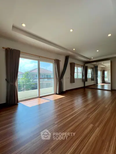 Spacious sunlit room with large windows and elegant wooden flooring in a modern home.