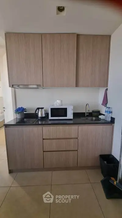Modern kitchen with sleek cabinetry and appliances, featuring a microwave and kettle on a black countertop.