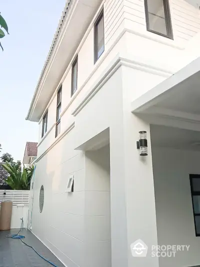 Elegant two-story residential home with a modern white facade, showcasing clean architectural lines and a spacious carport area, set against a clear sky.