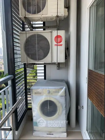 Compact balcony with washing machine and air conditioning units in urban apartment.