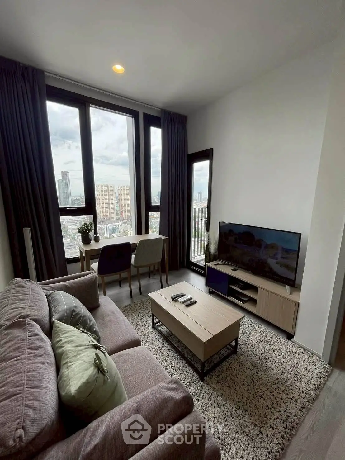 Modern living room with city view, cozy sofa, and entertainment setup in high-rise apartment.