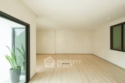 Spacious empty living room with wooden flooring and large windows, perfect for customization.
