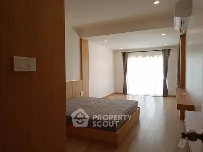 Spacious bedroom with wooden flooring and large window for natural light