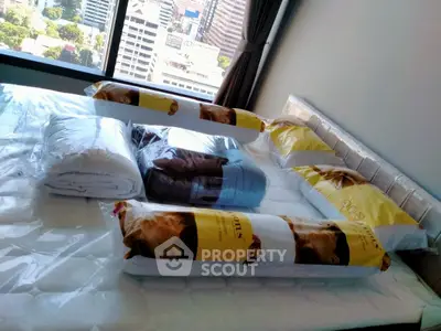 Spacious bedroom with large window offering city views, featuring a neatly arranged bed with pillows and comforters.