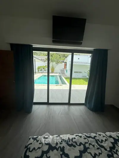 Luxurious bedroom with pool view through large glass doors, modern decor and elegant curtains.