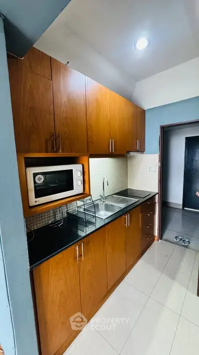 Modern kitchen with wooden cabinets and built-in microwave in a cozy apartment.