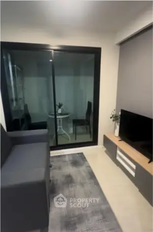 Modern living room with sleek furniture and glass sliding doors leading to a cozy balcony.