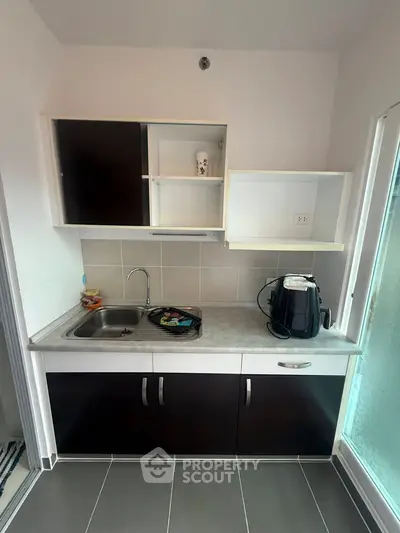 Compact kitchen with modern cabinets and countertop, featuring a sink and small appliances.