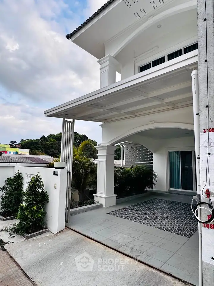 Elegant white exterior of a modern house with covered entrance and lush greenery.