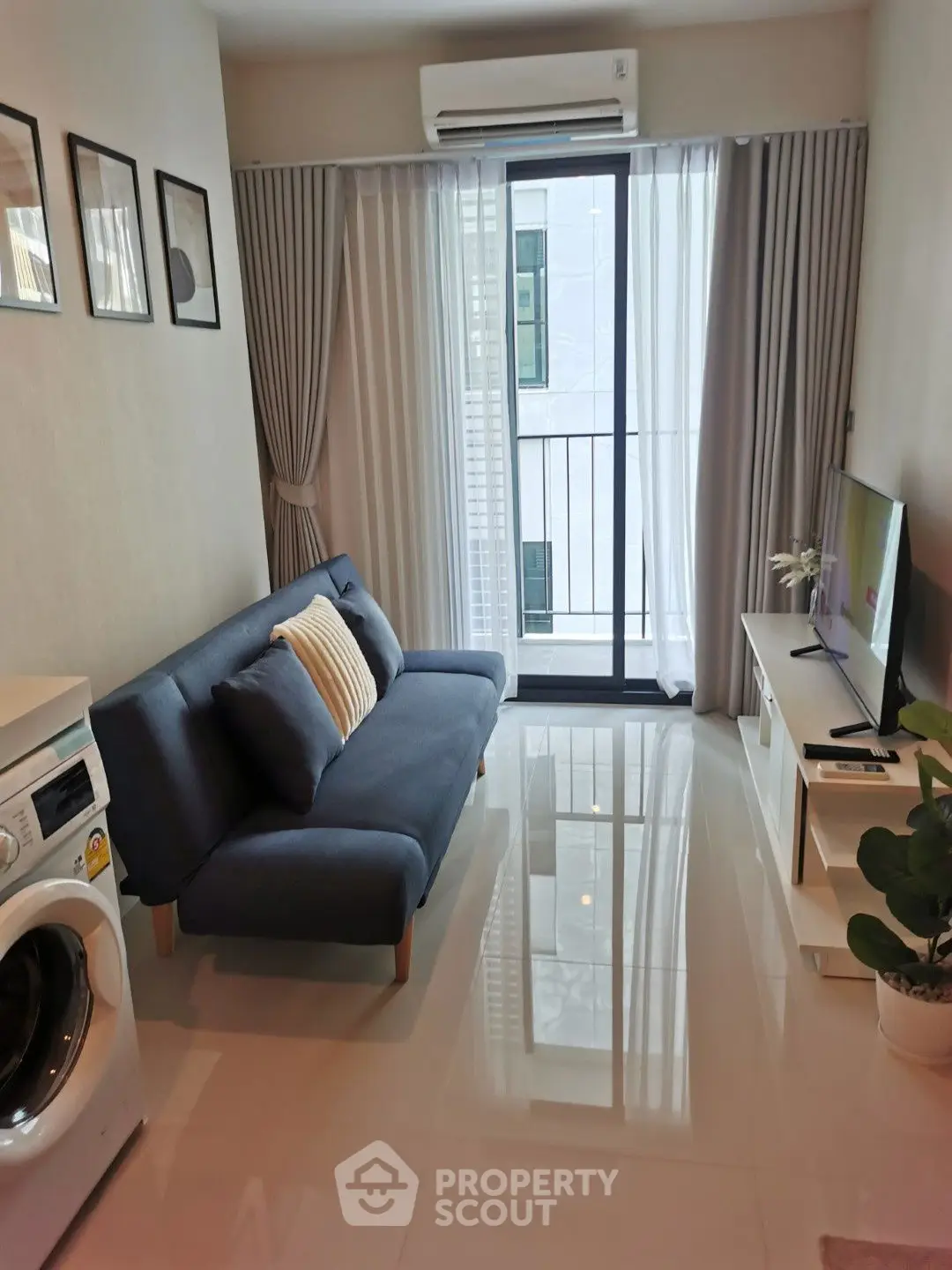 Modern living room with sleek sofa, TV, and washing machine near balcony.