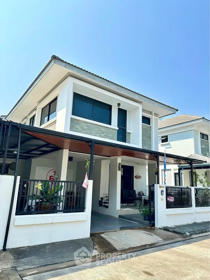 Modern two-story house with sleek design and spacious carport under clear blue sky.