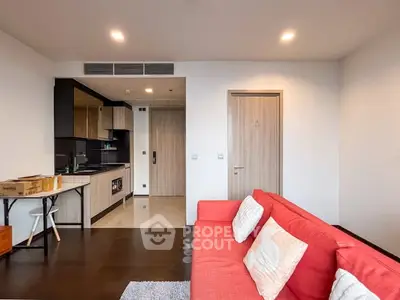 Modern living room with open kitchen, featuring red sofa and sleek design.