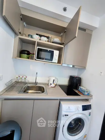Compact kitchen with microwave, washing machine, and ample storage in modern apartment.