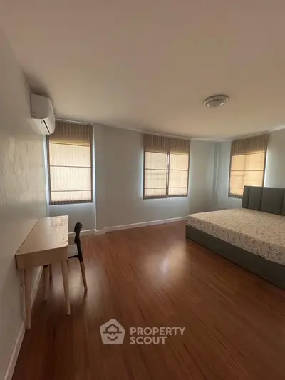 Spacious bedroom with wooden flooring and natural light
