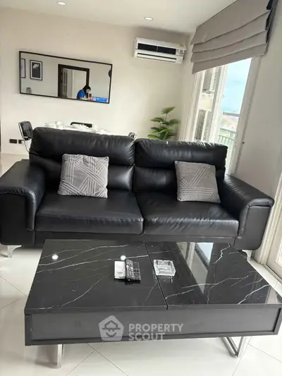 Modern living room with sleek black sofa and marble coffee table, featuring elegant decor and ample natural light.