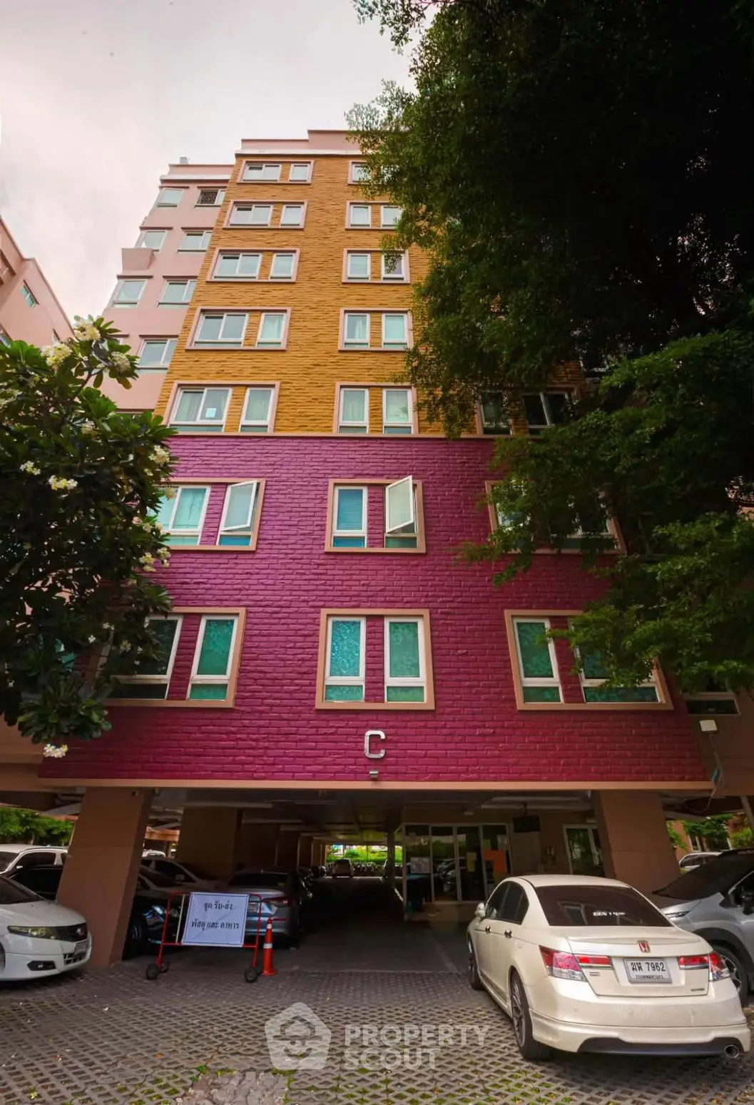 Colorful multi-story residential building with parking area and lush greenery.