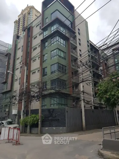 Modern urban apartment building with unique architectural design and multiple balconies in a bustling city area.
