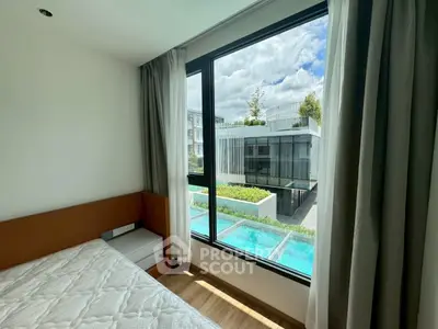 Modern bedroom with large window overlooking pool and contemporary building.