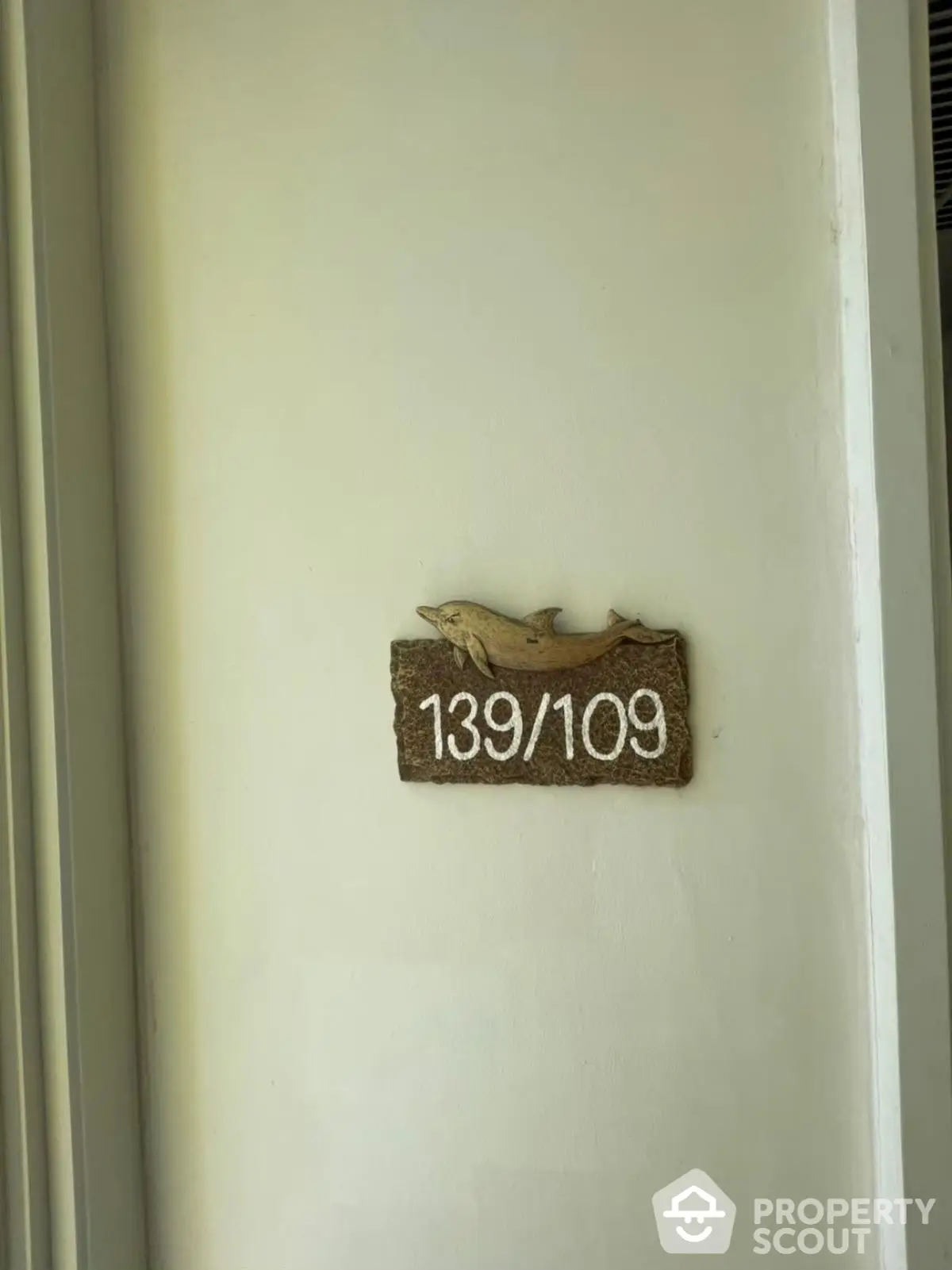 Apartment unit number sign with dolphin decoration on white wall.