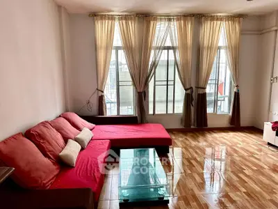 Spacious living room with red sofa and large windows for natural light.