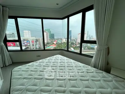 Spacious bedroom with panoramic city view from large corner windows, featuring a comfortable mattress.
