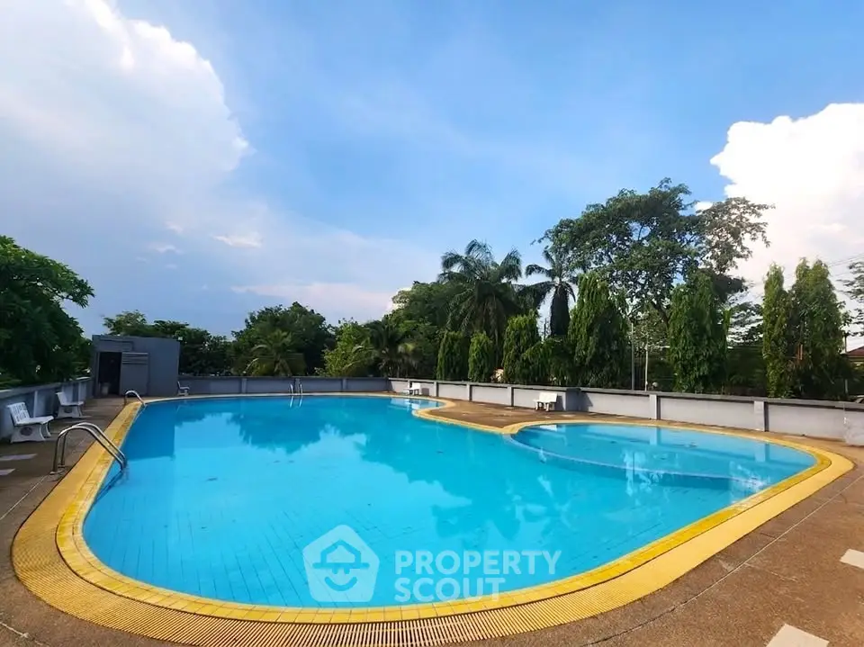 Luxurious outdoor swimming pool with lush greenery and clear blue sky, perfect for relaxation and leisure.