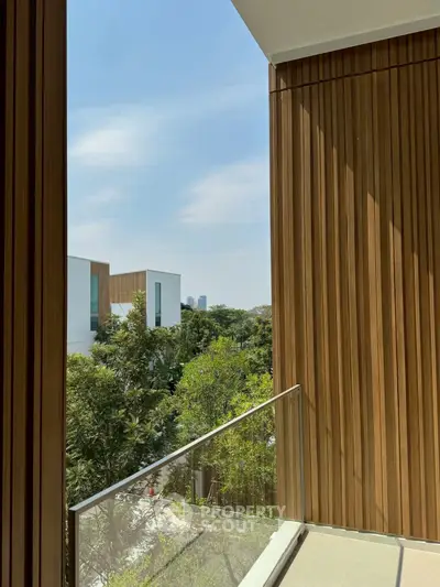 Modern balcony with wooden paneling and glass railing offering a serene view of greenery and cityscape.