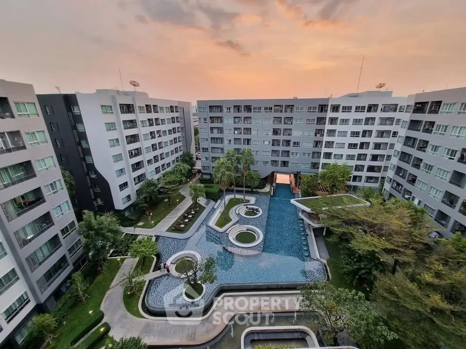 Stunning aerial view of modern apartment complex with lush gardens and elegant swimming pool at sunset.